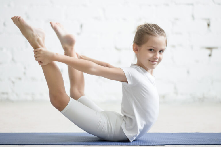 Smiling girl child in dhanurasana pose, white studio background